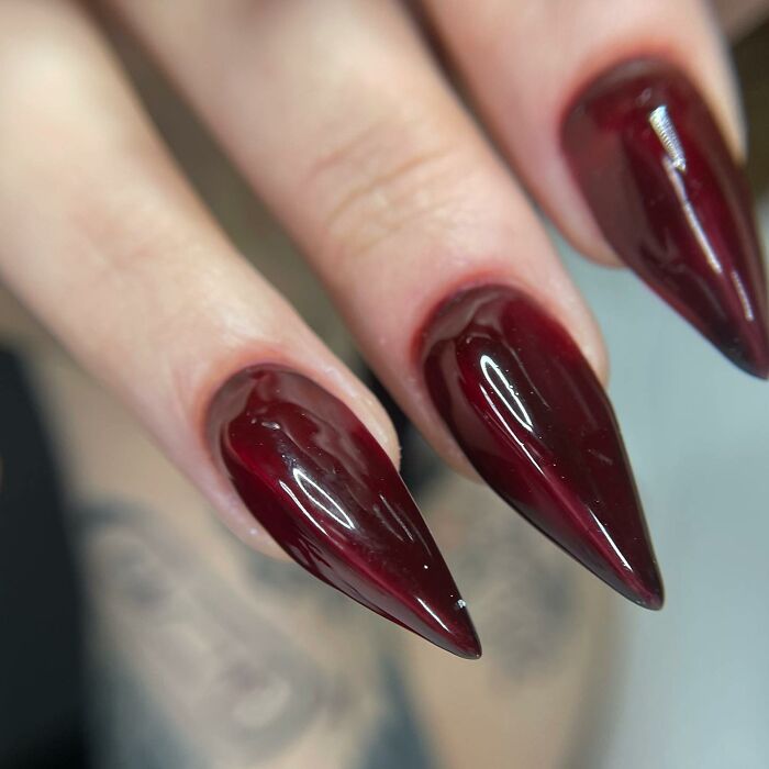 Glossy dark red stiletto nails with a unique swirl pattern, showcasing creative and bold nail designs that break all the rules.