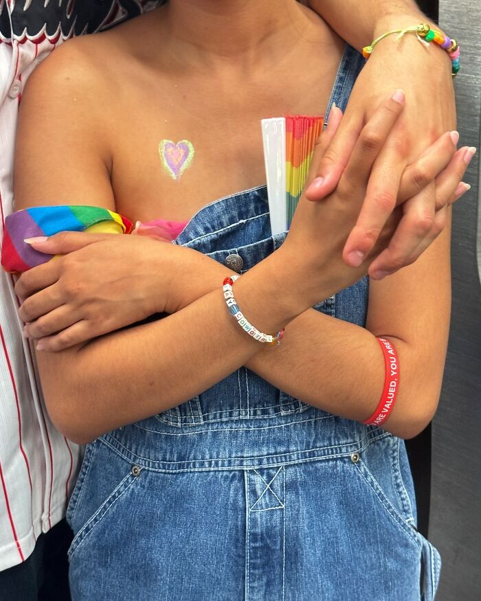 Two people on the New York subway with colorful bracelets and a rainbow fan, holding hands close together.