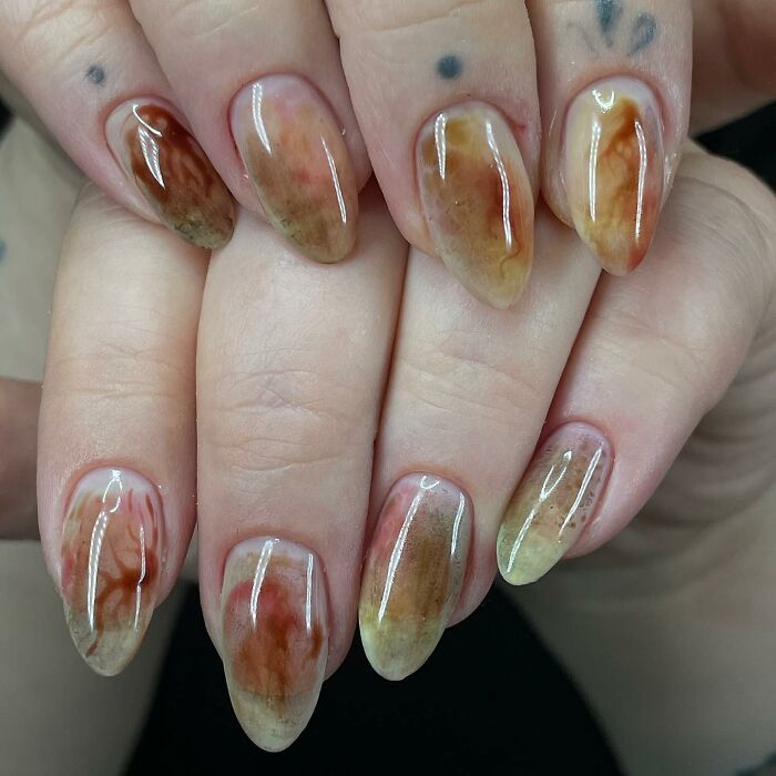 Glossy abstract nail designs with earthy tones on almond-shaped nails, showcasing unique and rule-breaking nail art creativity.