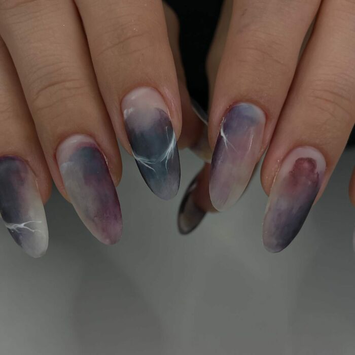 Hand with long nails featuring unique purple and white marble nail designs breaking all the rules with a stunning look.