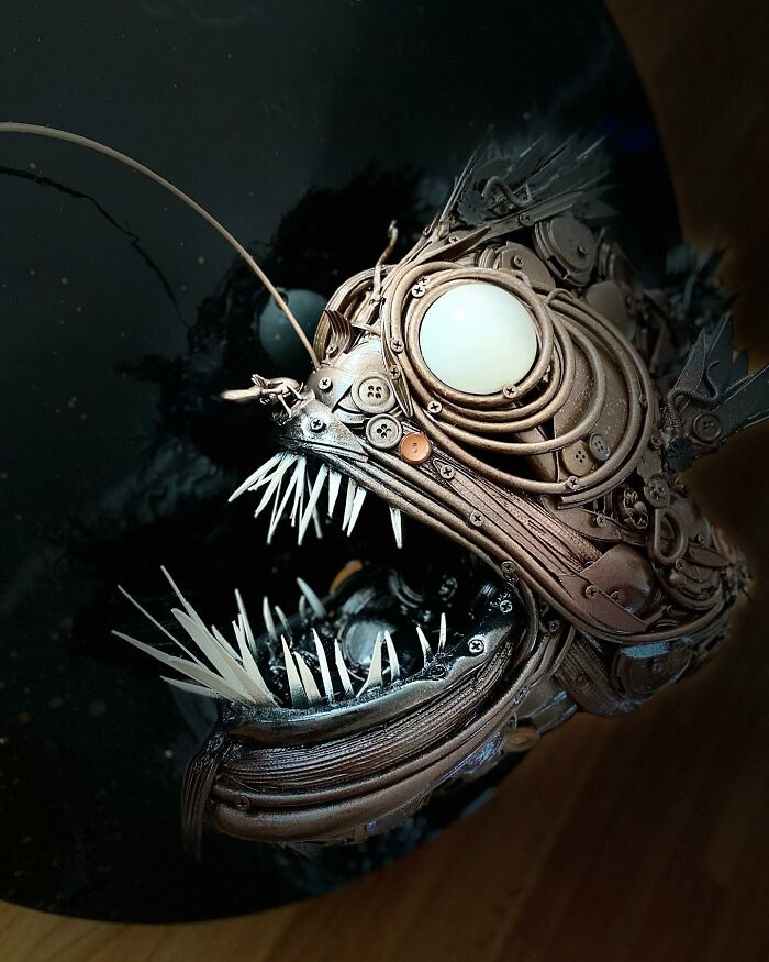 Stunning animal sculpture made from trash depicting an anglerfish with intricate mechanical details on a black circular background.