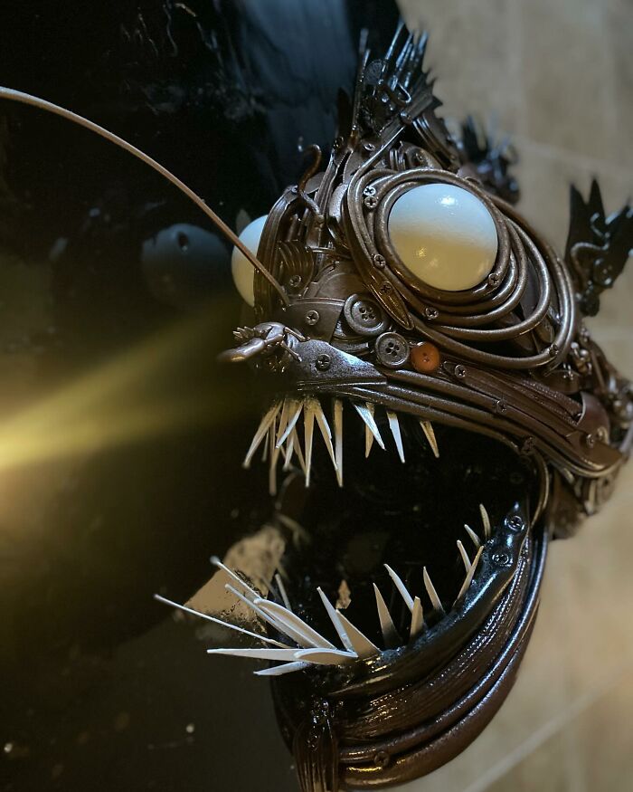 Stunning animal sculpture made from trash depicting an anglerfish with intricate mechanical details on a black circular background.