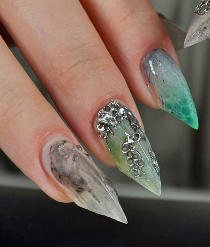 Stiletto nail designs featuring unique textures and metallic accents in muted green and gray tones.