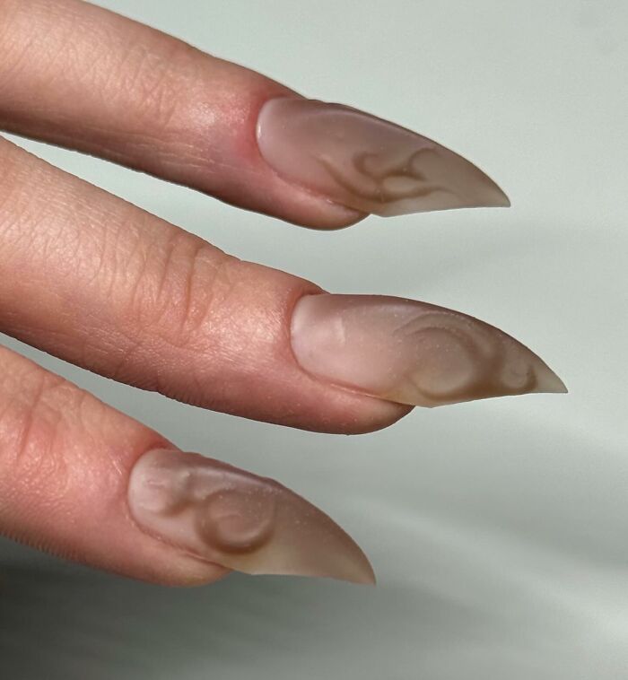 Matte stiletto nail designs in neutral tones with subtle abstract patterns showcasing unique nail art creativity.