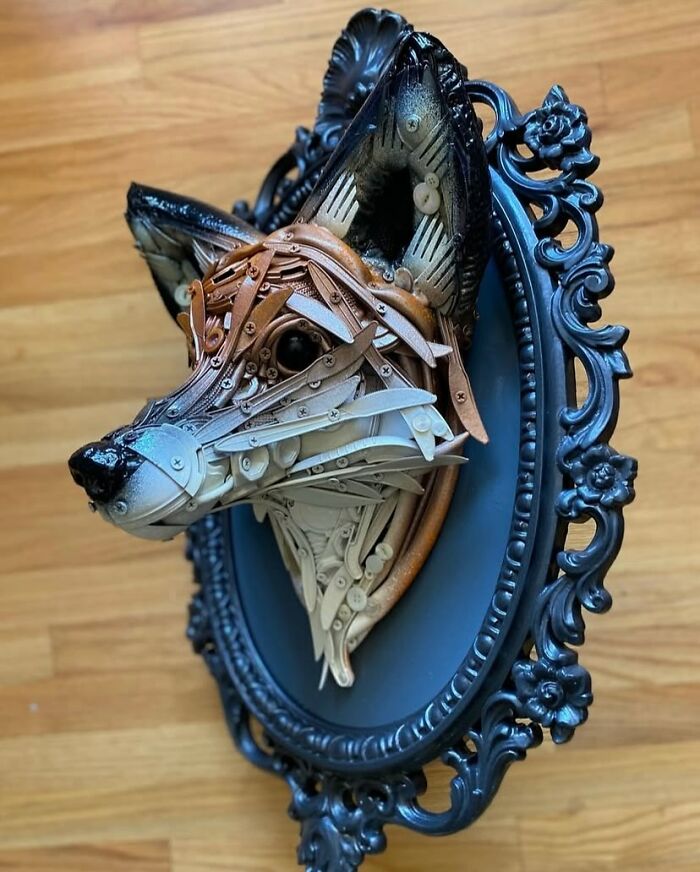 Fox animal sculpture made from recycled trash materials displayed in an ornate black frame on a wooden surface.