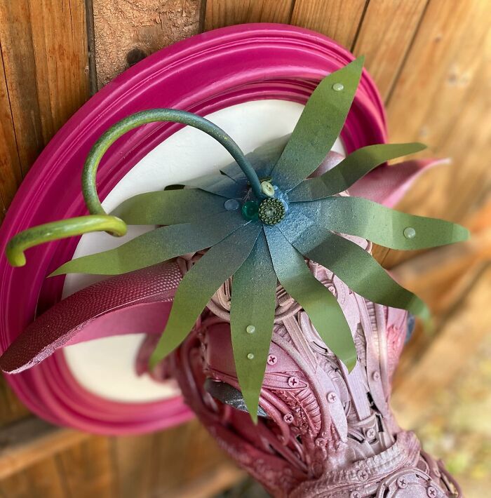 Pink animal sculpture made from trash, showcasing intricate details in a creative recycled art piece on a wooden floor.