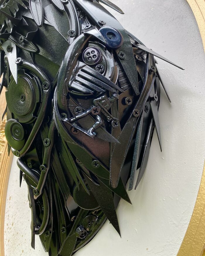 Recycled materials shaped into a stunning black bird sculpture mounted in an ornate gold frame on wooden wall.