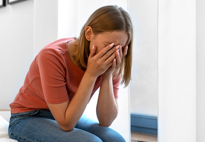 Young woman sitting indoors, covering her face, conveying emotions related to telling wife why daughter doesn’t trust. Young woman sitting indoors, covering her face, conveying emotions related to telling wife why daughter doesn’t trust.