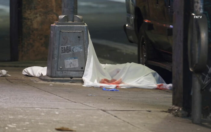 Covered body lies on a blood-stained city sidewalk near a vehicle, related to maniac driver shocking response incident.