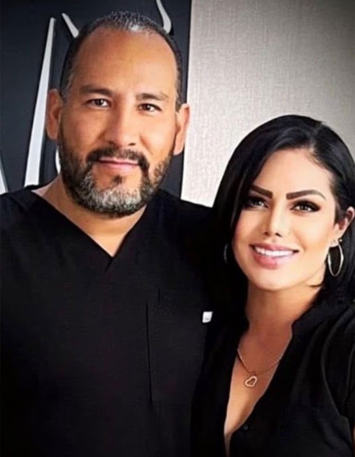 Surgeon who performed fatal breast enlargement and teen’s mom posing together, both dressed in black indoors. Surgeon who performed fatal breast enlargement and teen’s mom posing together, both dressed in black indoors.