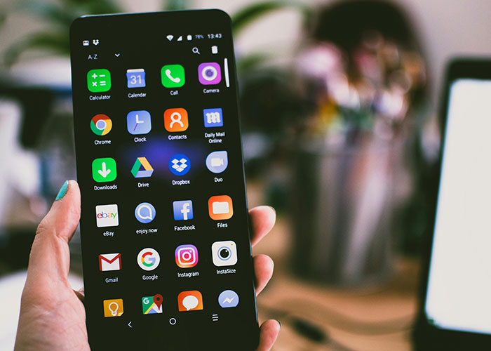 Hand holding smartphone displaying various apps, illustrating common purchases people have ditched due to high price tags.