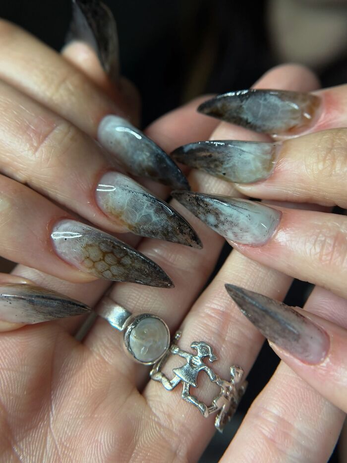 Long stiletto nail designs with smoky, translucent patterns and textured details creating an edgy, rule-breaking look.