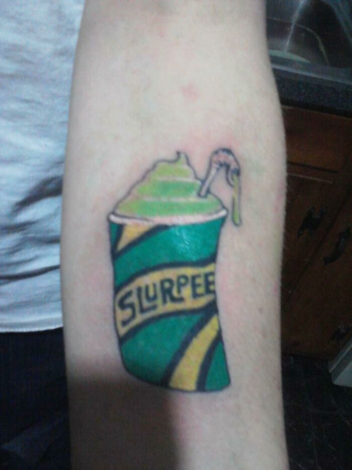 Tattoo of a slurpee cup with green and yellow stripes on a person's forearm, an example of worst client tattoo requests.