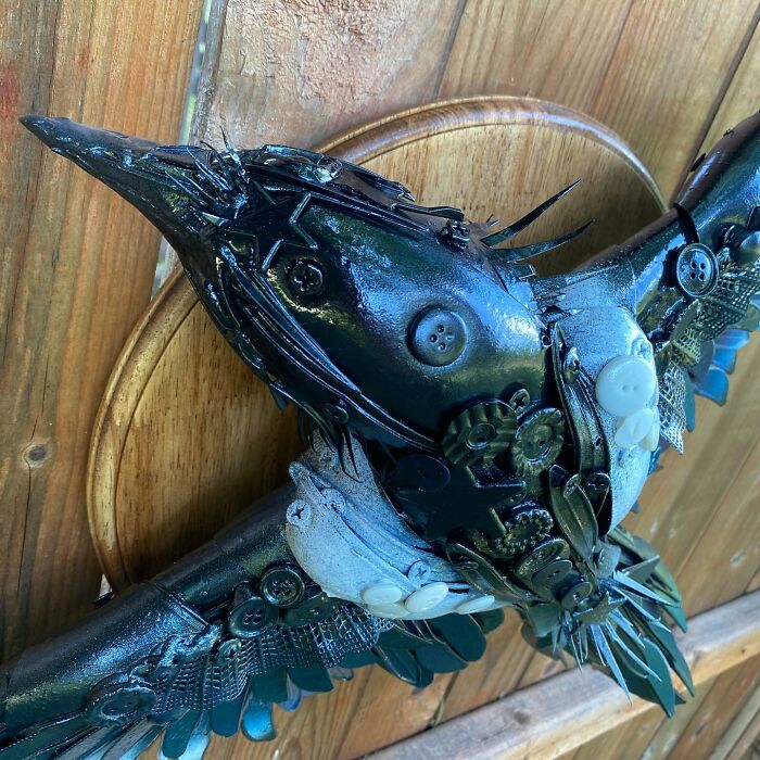 Intricate animal sculpture made from recycled trash materials resembling a bird with detailed wings mounted on wood.