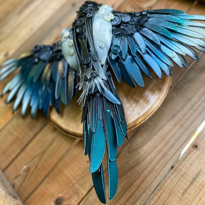 Intricate animal sculpture made from recycled trash materials resembling a bird with detailed wings mounted on wood.