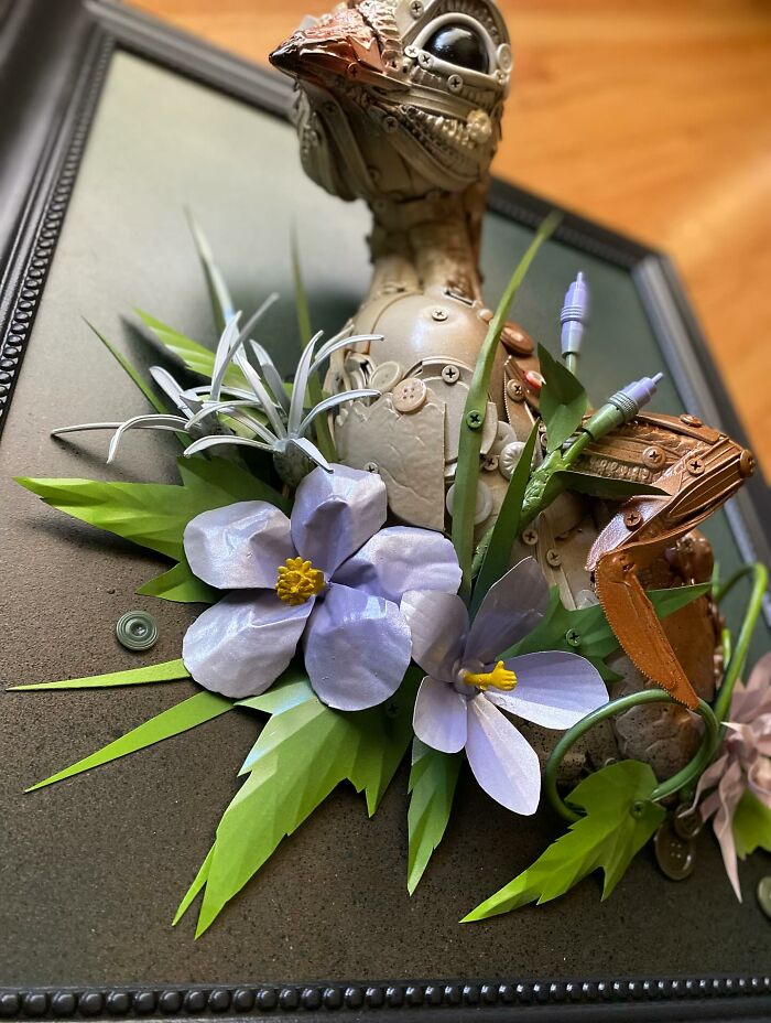 Steampunk style animal sculpture made from recycled trash and hardware, framed with green leaves and purple flowers.