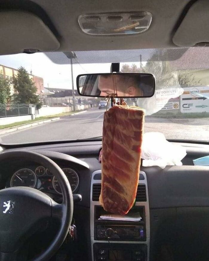 Car interior with a large piece of meat hanging from the rearview mirror, a unique meme from Eastern Europe culture.
