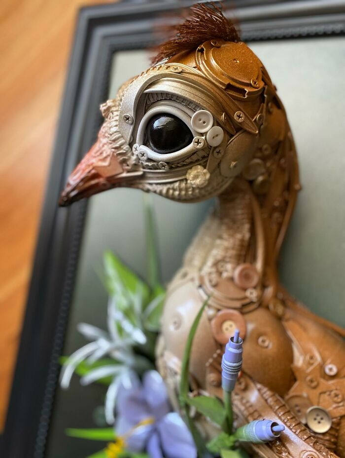 Steampunk style animal sculpture made from recycled trash and hardware, framed with green leaves and purple flowers.