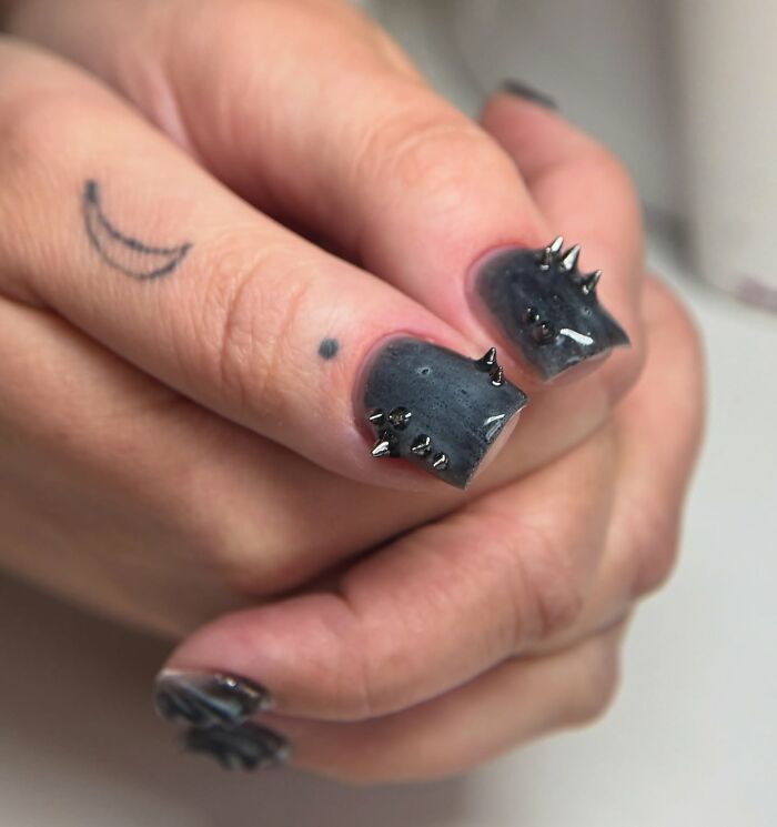 Glossy black and gray swirled nail designs with metallic spikes on short square nails, showcasing edgy nail design trends.