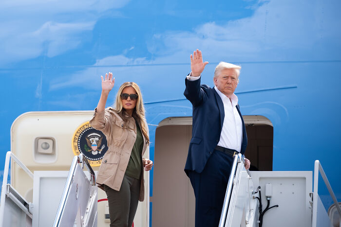 Donald Trump and Melania Trump waving on airplane stairs, body language experts analyzing finger-pointing exchange. Donald Trump and Melania Trump waving on airplane stairs, body language experts analyzing finger-pointing exchange.