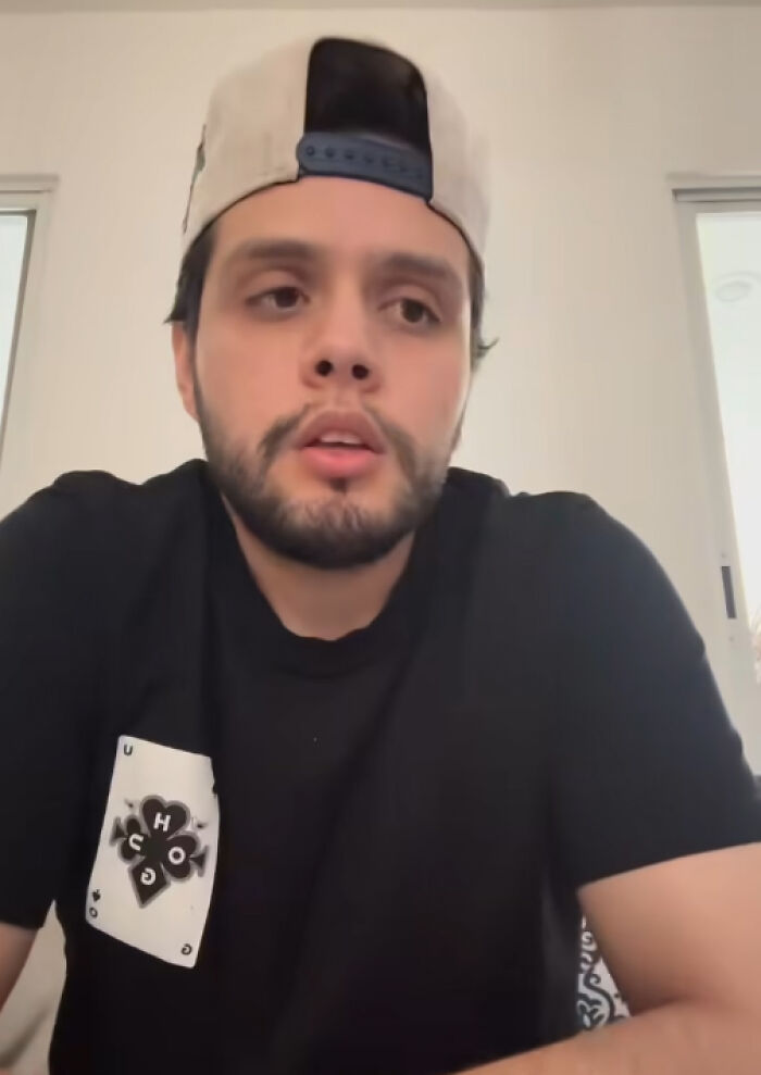 Young man wearing a black shirt and backward cap, appearing thoughtful in a bright indoor setting. Young man wearing a black shirt and backward cap, appearing thoughtful in a bright indoor setting.