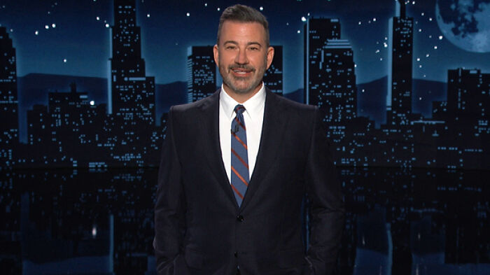Jimmy Kimmel standing on a nighttime city skyline set, wearing a dark suit and striped tie during a TV broadcast. Jimmy Kimmel standing on a nighttime city skyline set, wearing a dark suit and striped tie during a TV broadcast.