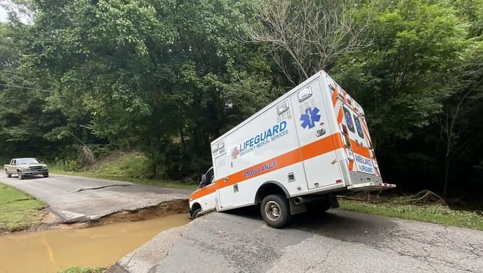 Ambulance partially stuck in a road sinkhole surrounded by trees, illustrating challenges faced by EMTs and paramedics.