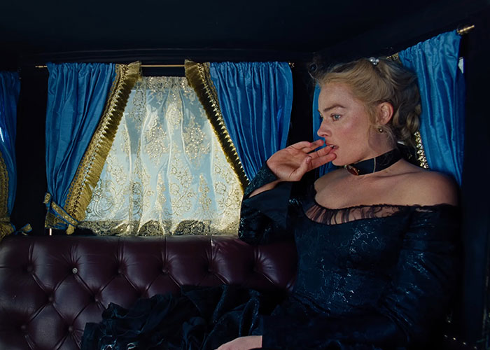 Margot Robbie in 1800s attire sitting in a vintage carriage with blue curtains, evoking Wuthering Heights atmosphere. Margot Robbie in 1800s attire sitting in a vintage carriage with blue curtains, evoking Wuthering Heights atmosphere.