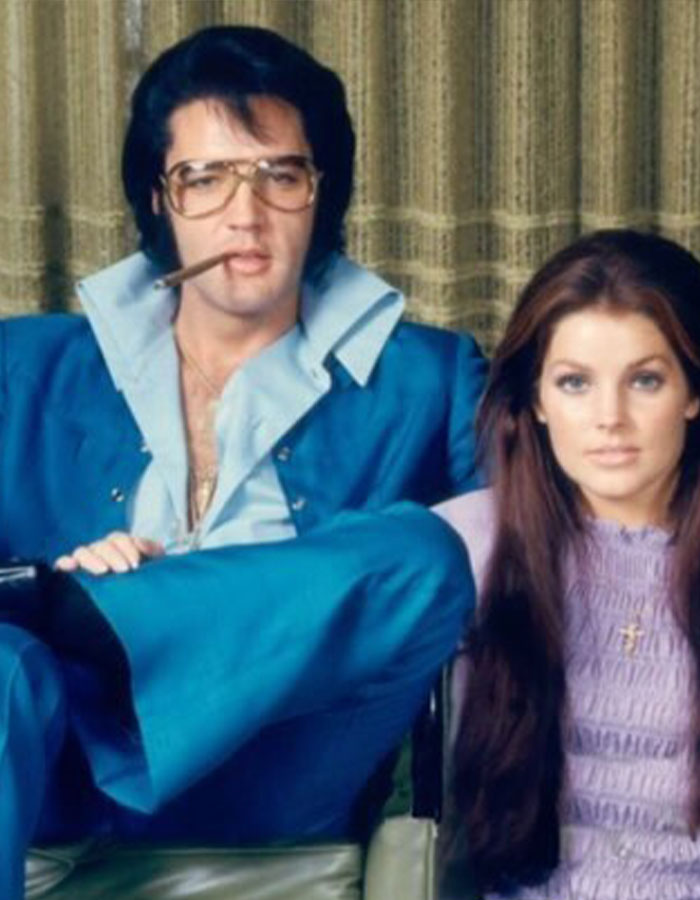 Elvis Presley in a blue suit smoking a cigar, sitting next to Priscilla Presley in a lavender top, vintage photo. Elvis Presley in a blue suit smoking a cigar, sitting next to Priscilla Presley in a lavender top, vintage photo.