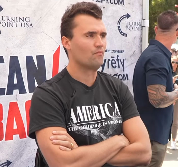 Man in black America shirt standing with arms crossed at a Turning Point USA event after NBC analyst fired for horrendous remarks Man in black America shirt standing with arms crossed at a Turning Point USA event after NBC analyst fired for horrendous remarks