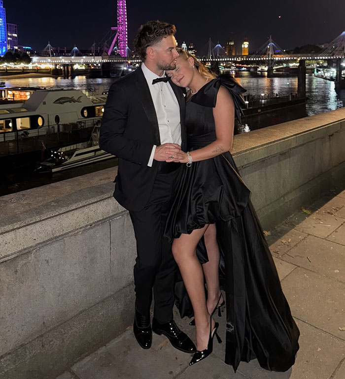 JoJo Siwa posing by the river at night, wearing a black dress, with a man in a tuxedo beside her. JoJo Siwa posing by the river at night, wearing a black dress, with a man in a tuxedo beside her.