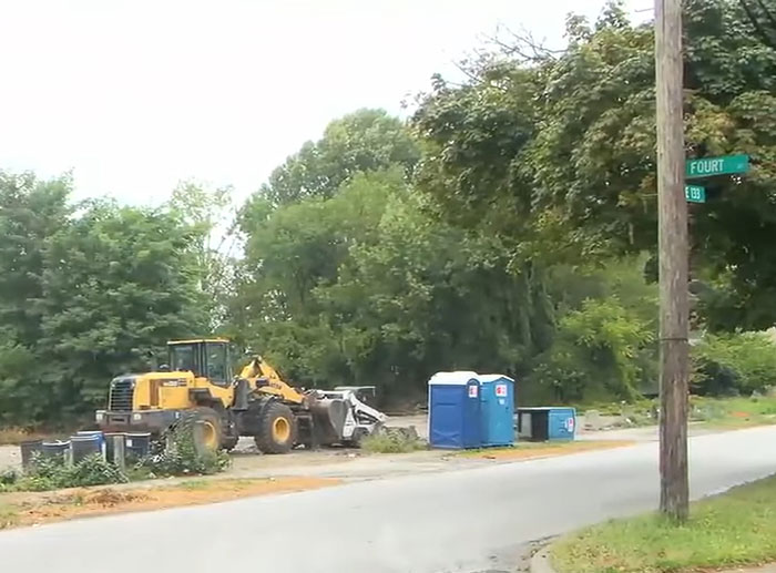 Construction site with porta-potty and heavy machinery near a street corner in a wooded suburban area. Construction site with porta-potty and heavy machinery near a street corner in a wooded suburban area.