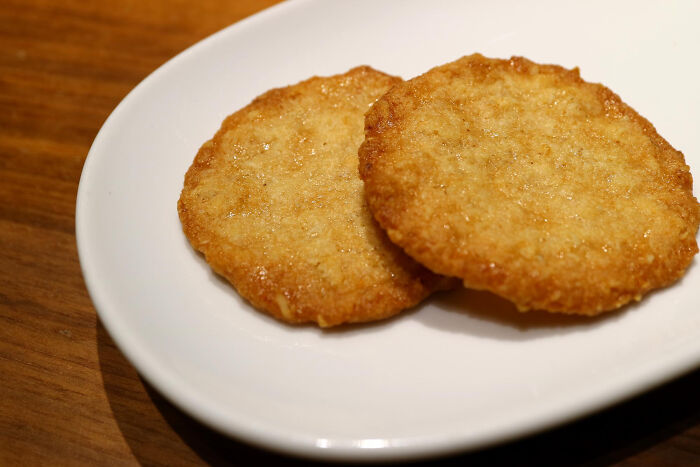 Two crispy hash brown patties served on a white plate on a wooden table, illustrating childish reasons ladies ditched a guy.