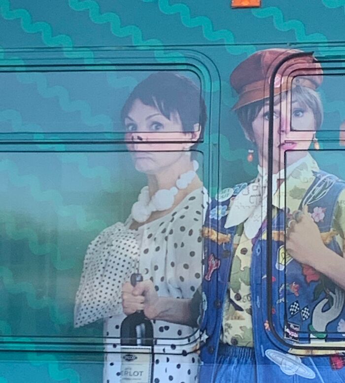 Bus advertisement placement fail showing two women, one holding a wine bottle, creating a humorous visual effect.