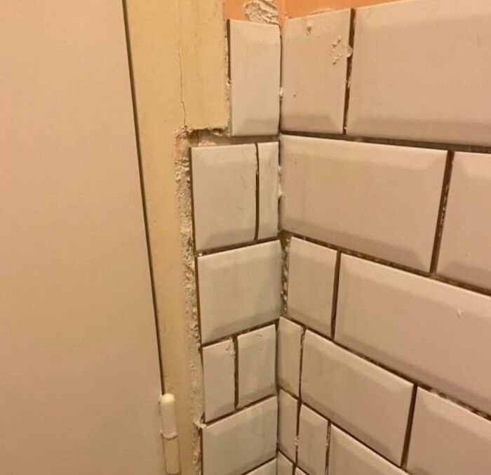 Uneven and poorly aligned tile construction with missing grout and rough edges near a door frame in a flawed design.