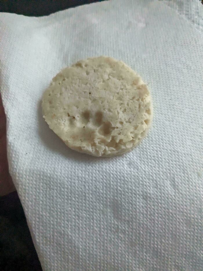 Round biscuit with a visible cute cat paw print pressed into its surface, placed on a white textured napkin.