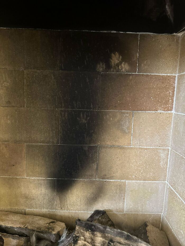Faint cute cat paw prints visible on soot-stained bricks above a fireplace with burnt logs below.