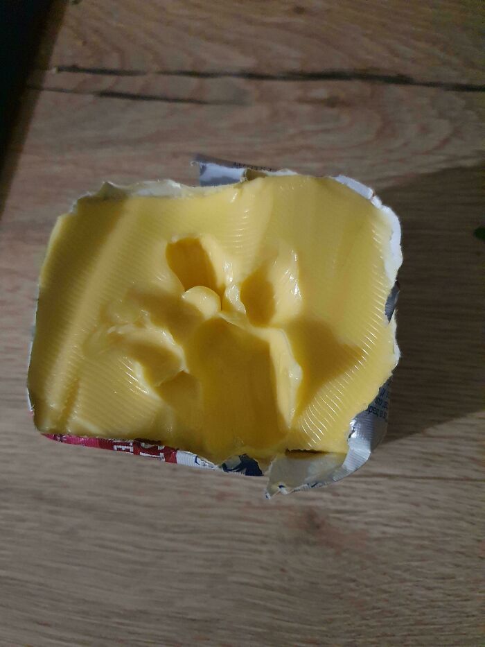 Cat paw prints pressed into soft butter on a wooden surface showcasing cute cat paw prints detail.