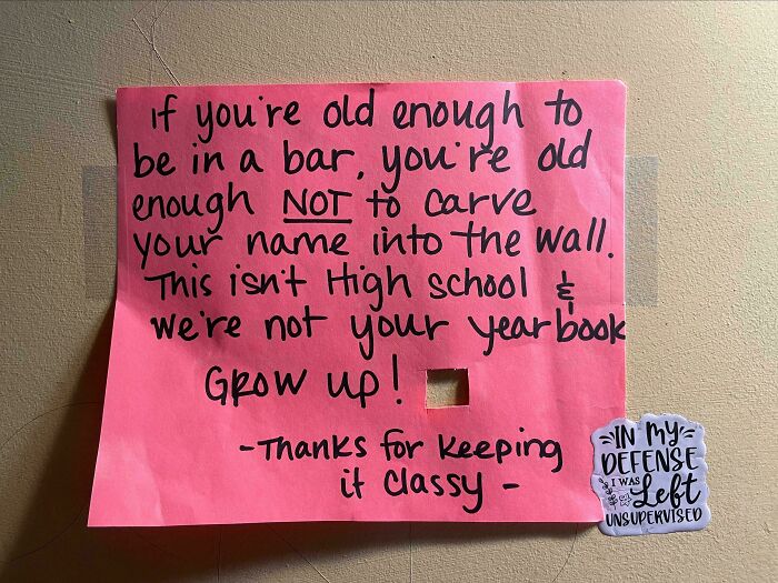 Funny handwritten note on a pink paper humorously telling people not to carve names on the wall, reminding us not to take life too seriously.