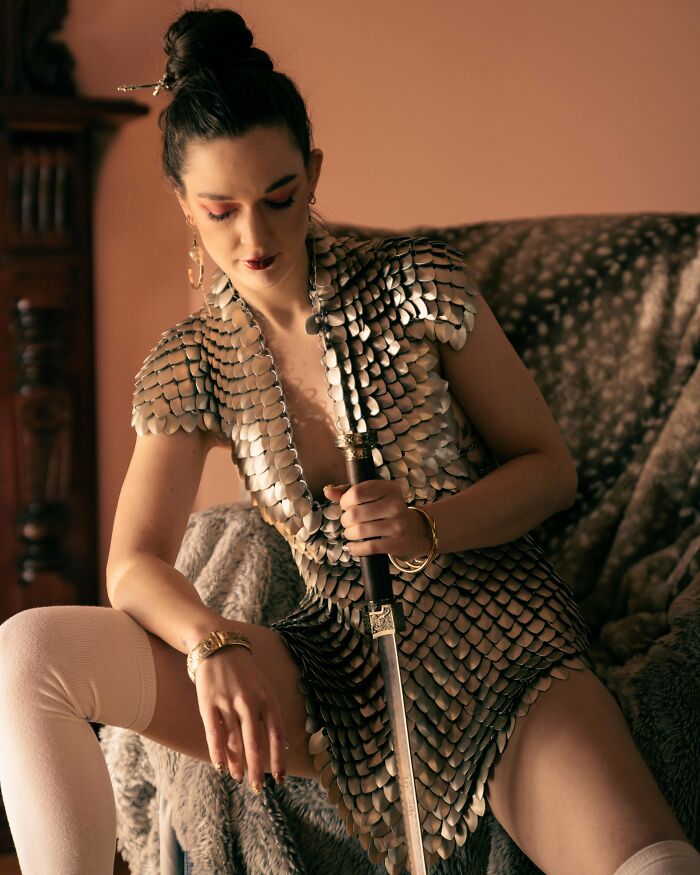 Woman wearing a cool scale armor dress holding a sword, showcasing something people made that is impressive and creative.