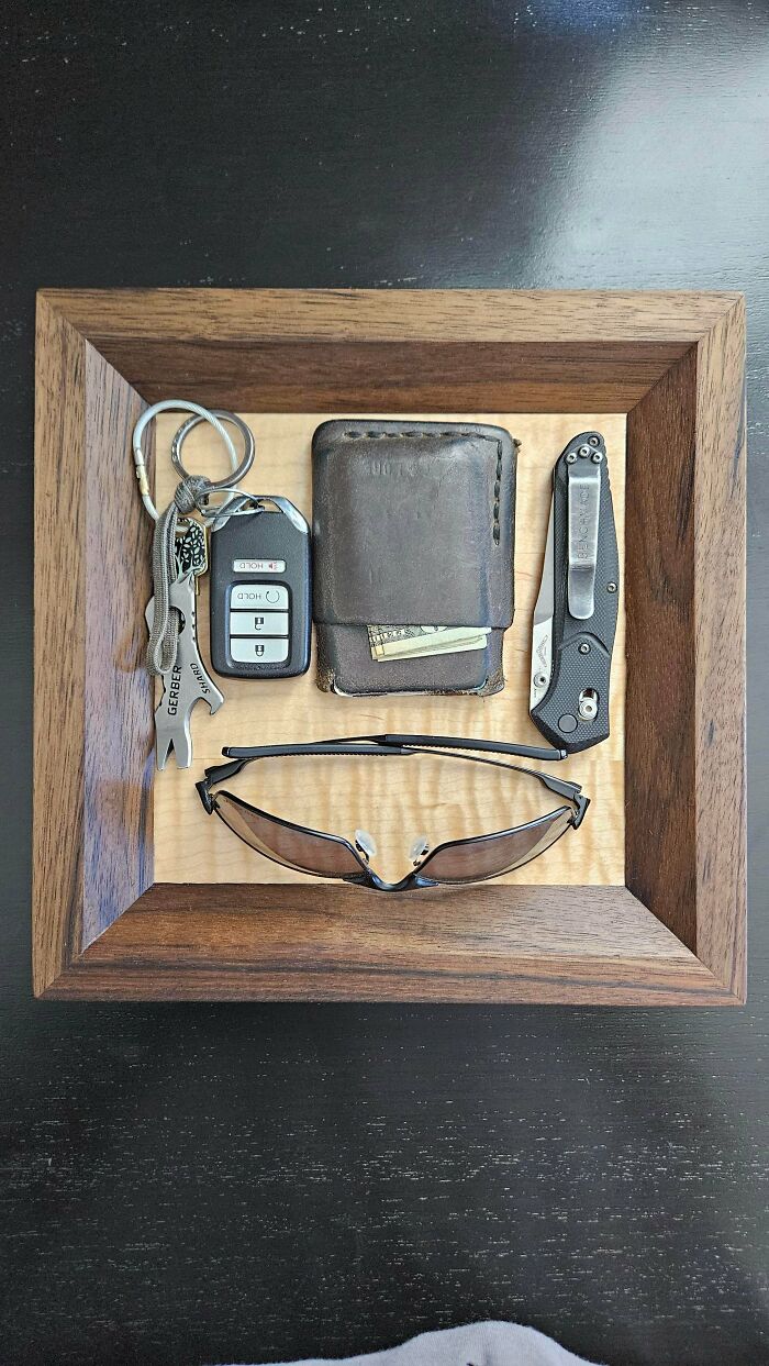 Woodworker-carved wooden tray displaying everyday carry items including keys, wallet, knife, and sunglasses on a polished surface.