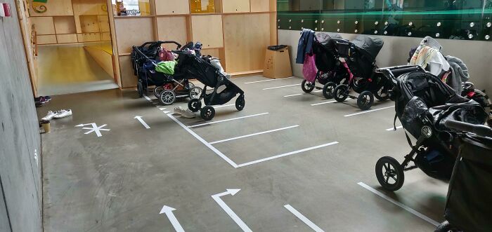 Modern Danish prison cell play area with baby strollers neatly parked on marked concrete floor.