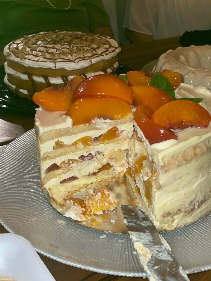 Layered peach cake with creamy filling and fresh peach slices, showcasing beautiful baked goods in a kitchen setting.