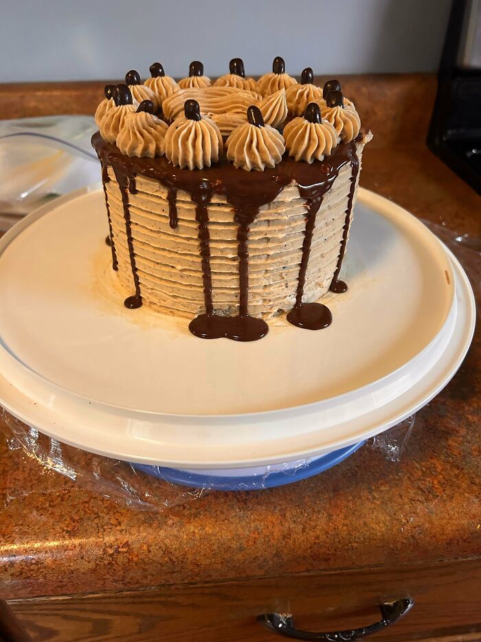 Chocolate drip cake with piped frosting and chocolate decorations on a white plate showcasing gorgeous baked goods.