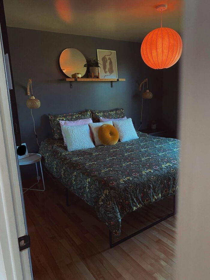Cozy bedroom with floral bedspread, decorative pillows, round mirror, warm pendant light, and modern home decoration.