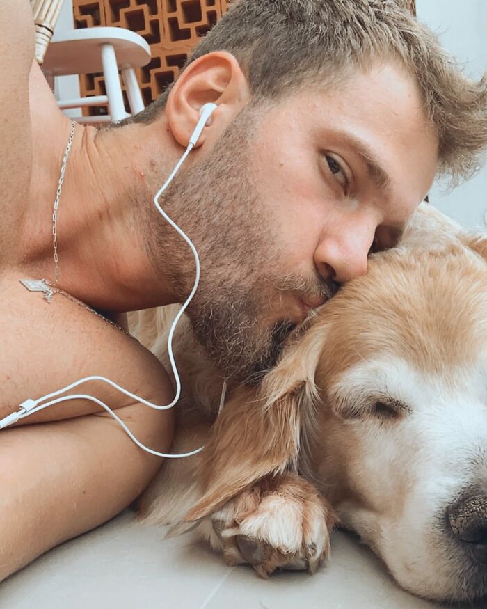 Man wearing earphones lying close and kissing a golden retriever, showing a moment of affection and connection. Man wearing earphones lying close and kissing a golden retriever, showing a moment of affection and connection.