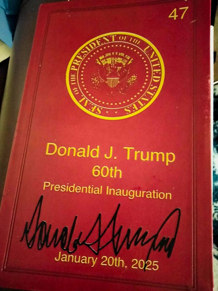 Red booklet cover with presidential seal, titled Donald J. Trump 60th Presidential Inauguration, signed and dated January 20, 2025.