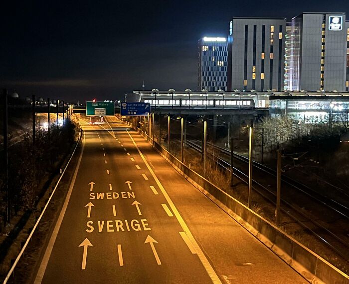 Night view of a Danish prison cell area near highway signs pointing to Sweden and Sverige destinations.