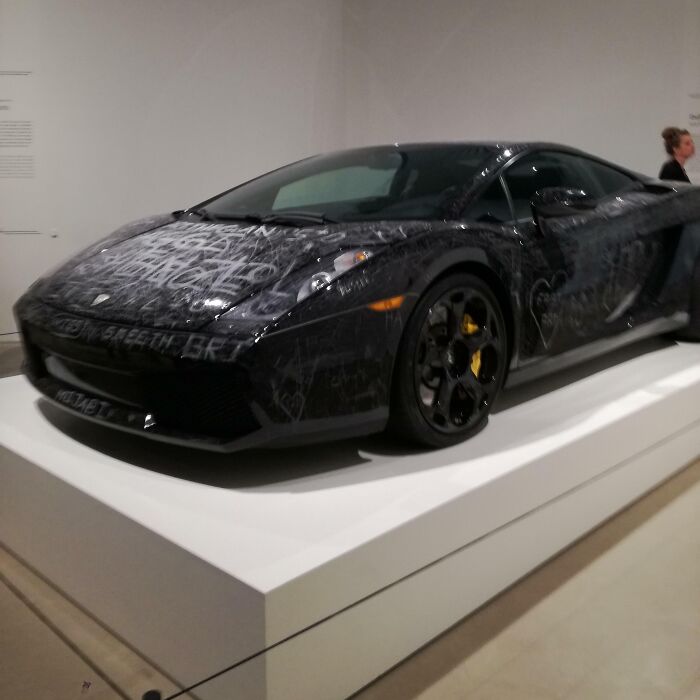Black sports car with graffiti-like markings displayed indoors on a white platform, highlighting Danish design and innovation.