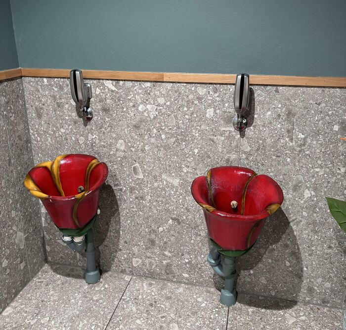 Colorful flower-shaped urinals in a Danish prison cell with gray stone walls and mounted soap dispensers.